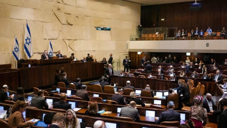 מליאת הכנסת בזמן דיון, חברי כנסת יושבים ליד שולחנותיהם ודגלי ישראל מוצגים ברקע.